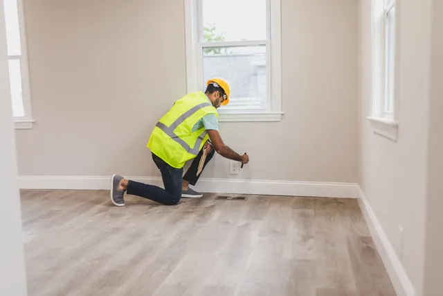 Technician checking the base of a wall for moisture in an empty room